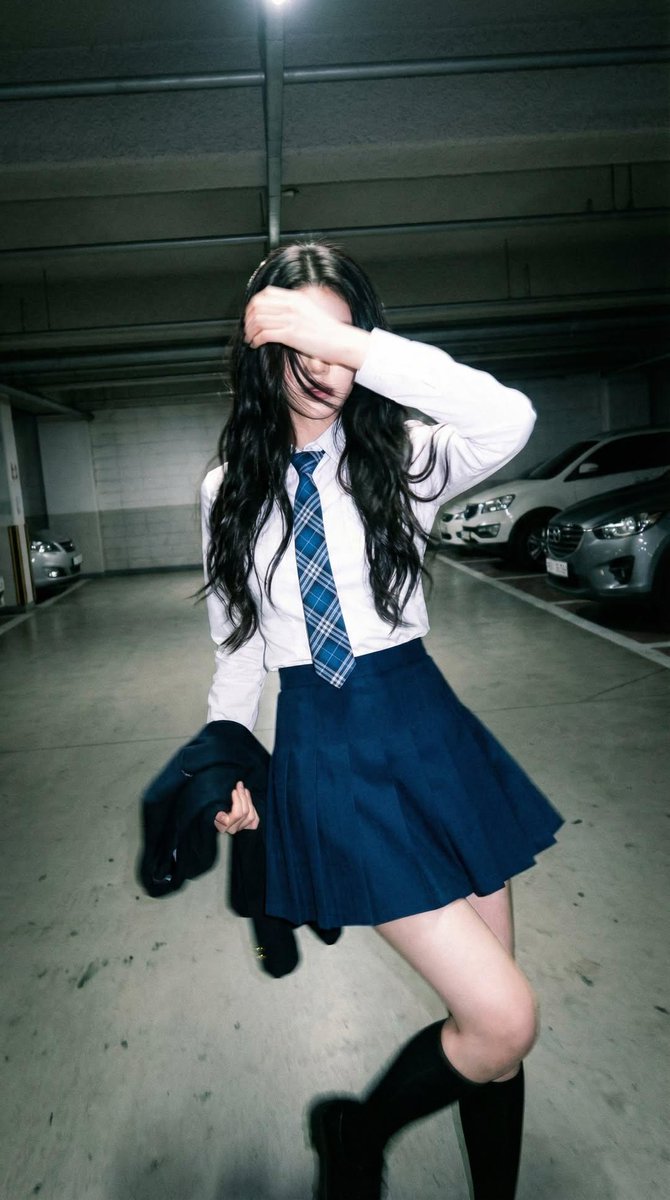 Candid portrait of a young woman in a dim parking garage, wearing a white shirt with a blue plai 2