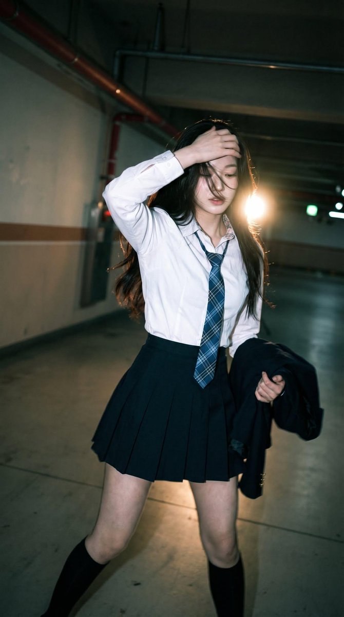 Candid portrait of a young woman in a dim parking garage, wearing a white shirt with a blue plai